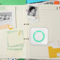 PocketLabel pocket thermal printer on a scrapbook page beside printed photos and notes