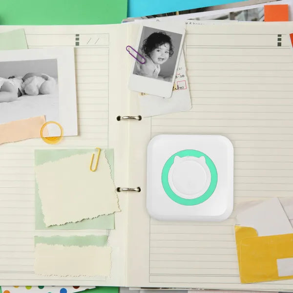 PocketLabel pocket thermal printer on a scrapbook page beside printed photos and notes